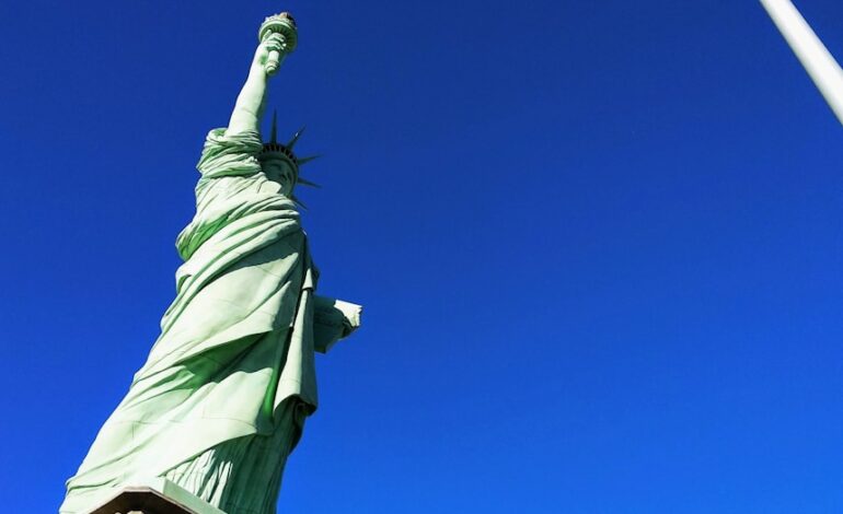 Statue of Liberty in front USA flag under blue sky